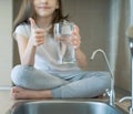 Little child drinking from water tap or faucet in kitchen. Young girl showing thumbs up sign and holding a transparent glass. Kid