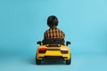 Little child driving yellow toy car on light blue background, back view Royalty Free Stock Photo