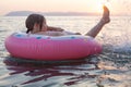 Little child floating at the ocean with pink inflatable ring against sunset sun light