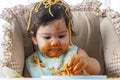 Little child funny girl eating spaghetti with spoon while sitting in high-powered chair at home. Toddler child with Royalty Free Stock Photo