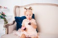 Little child girl in beautiful dress eats cake while sitting on sofa in living room. The princess in pink dress holds festive Royalty Free Stock Photo