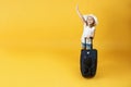 Little child girl blonde ready for the journey, standing with a suitcase and hand outstretched up. Yellow background Royalty Free Stock Photo