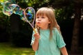 Little child, girl blowing huge bubbles alone, portrait outdoors. Young kid with puffed cheeks blows big bubbles outside, closeup