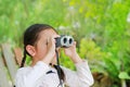 Little child girl in a field looking through binoculars in nature outdoor. Explore and adventure concept