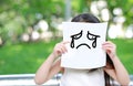 Little child girl holding up a white paper with draw crying face expression in nature park