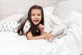 Little child girl lies in bed uses digital tablet. Royalty Free Stock Photo