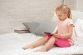 Little child girl lies in bed uses digital tablet. Royalty Free Stock Photo