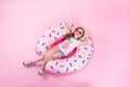 A little child girl lying on a donut inflatable circle. Pink background. Top view. Summer concept