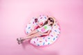 A little child girl lying on a donut inflatable circle. Pink background. Top view. Summer concept