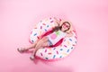 A little child girl lying on a donut inflatable circle. Pink background. Top view. Summer concept