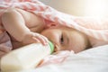 Little child girl lying on white bed and drinking milk from bottle Royalty Free Stock Photo