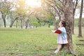 Little child girl reading book in summer park outdoor standing lean against tree trunk with looking to sky Royalty Free Stock Photo