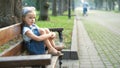 Little child girl sitting alone on a bench in summer park Royalty Free Stock Photo