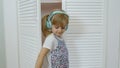 Little child girl wearing headphones listening to music and funnily dancing near wardrobe at home
