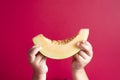 Little child hand holding a honeydew melon or rockmelon against pink background.