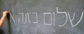 Little child hand writes Hello First Grade greetings in Hebrew