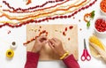 Little child hands make necklace with colorful seeds and forest berries.