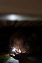 Little child, hiding under the bed, hugging teddy bear and holding flashlight Royalty Free Stock Photo