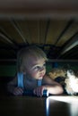 Little child, hiding under the bed, hugging teddy bear and holding flashlight Royalty Free Stock Photo