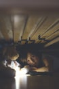 Little child, hiding under the bed, hugging teddy bear and holding flashlight Royalty Free Stock Photo