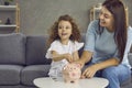 Happy young mother and little daughter putting coins in their piggy bank together Royalty Free Stock Photo