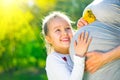 Little child listening baby in belly of her mother outdoor in sunny nature. Happy pregnant mother with her little daughter