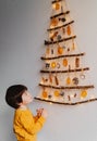 Little child looking at handmade craft Christmas tree made from sticks and natural materials hanging on wall.