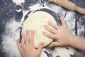 Little child making dough for backing. Kid`s hands, some flour, wheat dough and rolling-pin on the black table. Children hands ma