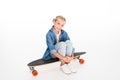 Little child in oversized denim shirt sitting on a longboard,