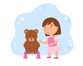 A little child in a pink dress is playing doctor with a teddy bear. Cute baby vaccinates toy