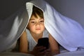 Little child play on smart phone in bed under the covers at nigh Royalty Free Stock Photo