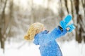 Little child playing with fresh snow in winter park. Cute funny boy throws snow up. Baby wearing a warm clothing, hat, scarf.