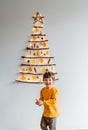 Little child playing with handmade craft Christmas tree made from sticks and natural materials hanging on wall.