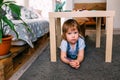 Little child playing hide and seek at home under the children's table. Royalty Free Stock Photo