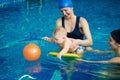 Little child playing in swimming pool. Baby staying on water on board, trying getting orange rubber ball in blue water