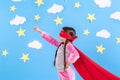 Little child plays superhero. Kid on the background of bright blue wall with white clouds and stars . Girl power concept Royalty Free Stock Photo