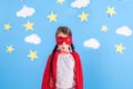 Little child plays superhero. Kid on the background of bright blue wall with white clouds and stars . Girl power concept Royalty Free Stock Photo