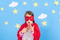 Little child plays superhero. Kid on the background of bright blue wall with white clouds and stars . Girl power concept Royalty Free Stock Photo