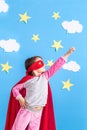 Little child plays superhero. Kid on the background of bright blue wall with white clouds and stars . Girl power concept Royalty Free Stock Photo