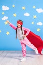 Little child plays superhero. Kid on the background of bright blue wall with white clouds and stars . Girl power concept Royalty Free Stock Photo