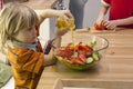 Little child pouring olive oil into mixed salad.