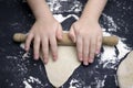 Little child preparing dough for backing. Kid`s hands, some flour, wheat dough and rolling-pin on the black table. Children hands Royalty Free Stock Photo