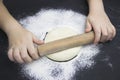 Little child preparing dough for backing pie. Kid`s hands, some flour, wheat dough and rolling-pin on black table. Children hands Royalty Free Stock Photo