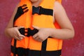 Little child putting on orange life vest near red wall, closeup Royalty Free Stock Photo