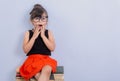 Little child reading book and in bewilderment covers mouth. Kid with glasses sitting on books. Royalty Free Stock Photo