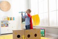 Little child in red cape playing with ship made of cardboard box