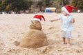 Little child in red santa hat with sand snowman on beach Royalty Free Stock Photo