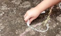 Little child`s hand, girl holding white chalk, drawing, writing on the concrete outside. School age kid drawing with chalk