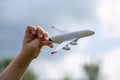 Little child`s hand holds white metal airplane model pretending he is flying Boing plane in clear blue sky with clean white fluff