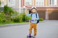 Little child in safety helmet riding scooter to school. Cute boy waving hand saying hi. Safety kids by way to school